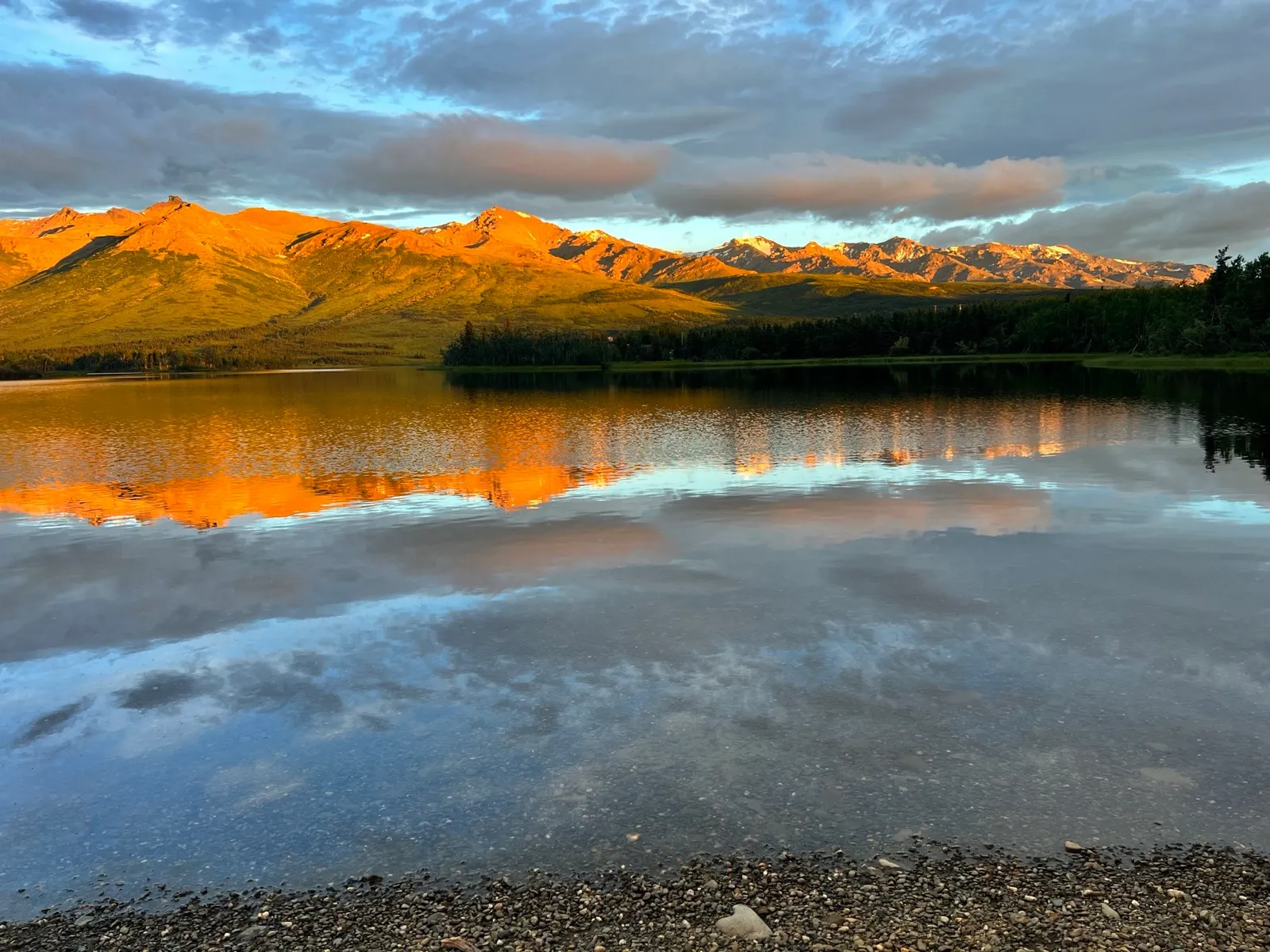 Mountains glowing orange in alpenglow, mirrored almost perfectly in the still surface of a small reflection pond.